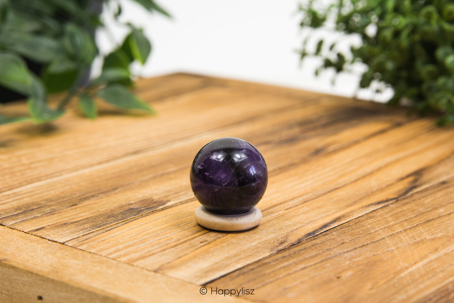Amethyst crystal ball on a wooden surface with greenery in the background