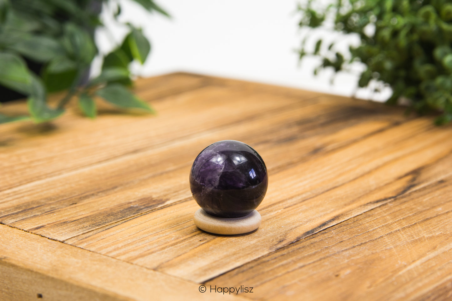 Amethyst crystal ball on a wooden surface with greenery in the background