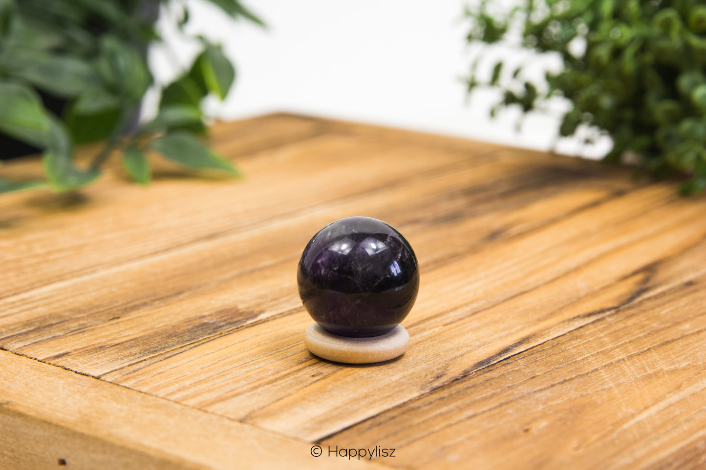 Purple amethyst sphere on a wooden surface with green plants in the background