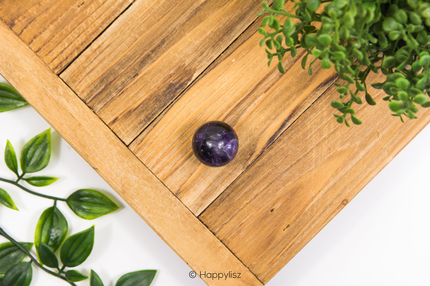 Purple amethyst crystal on a wooden surface with green leaves