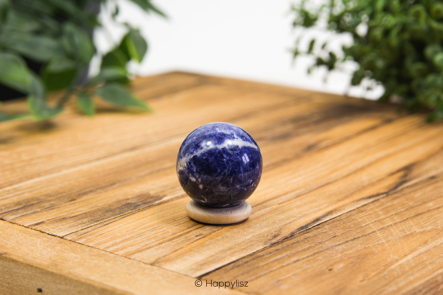 Sodalite spherical object on a wooden surface with greenery in the background