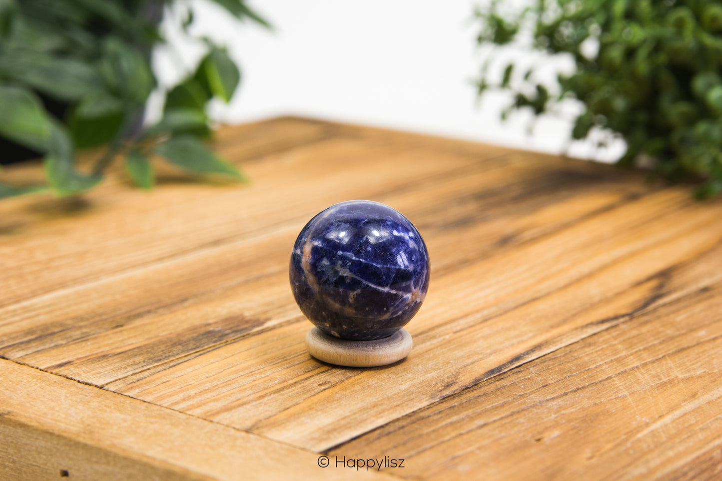 Marble-like blue sphere on a wooden surface with greenery in the background