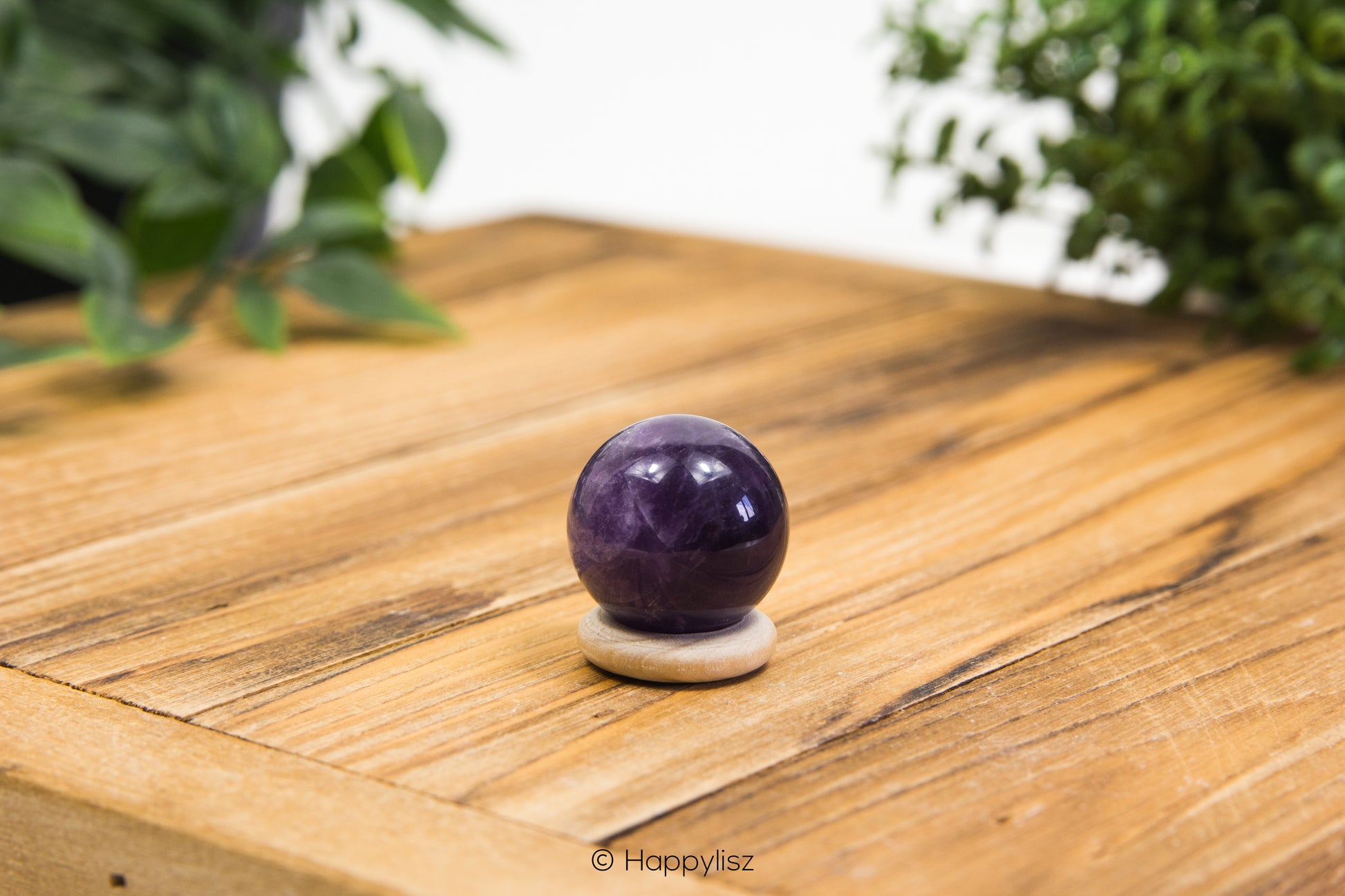 Purple crystal ball on a wooden surface with green plants in the background