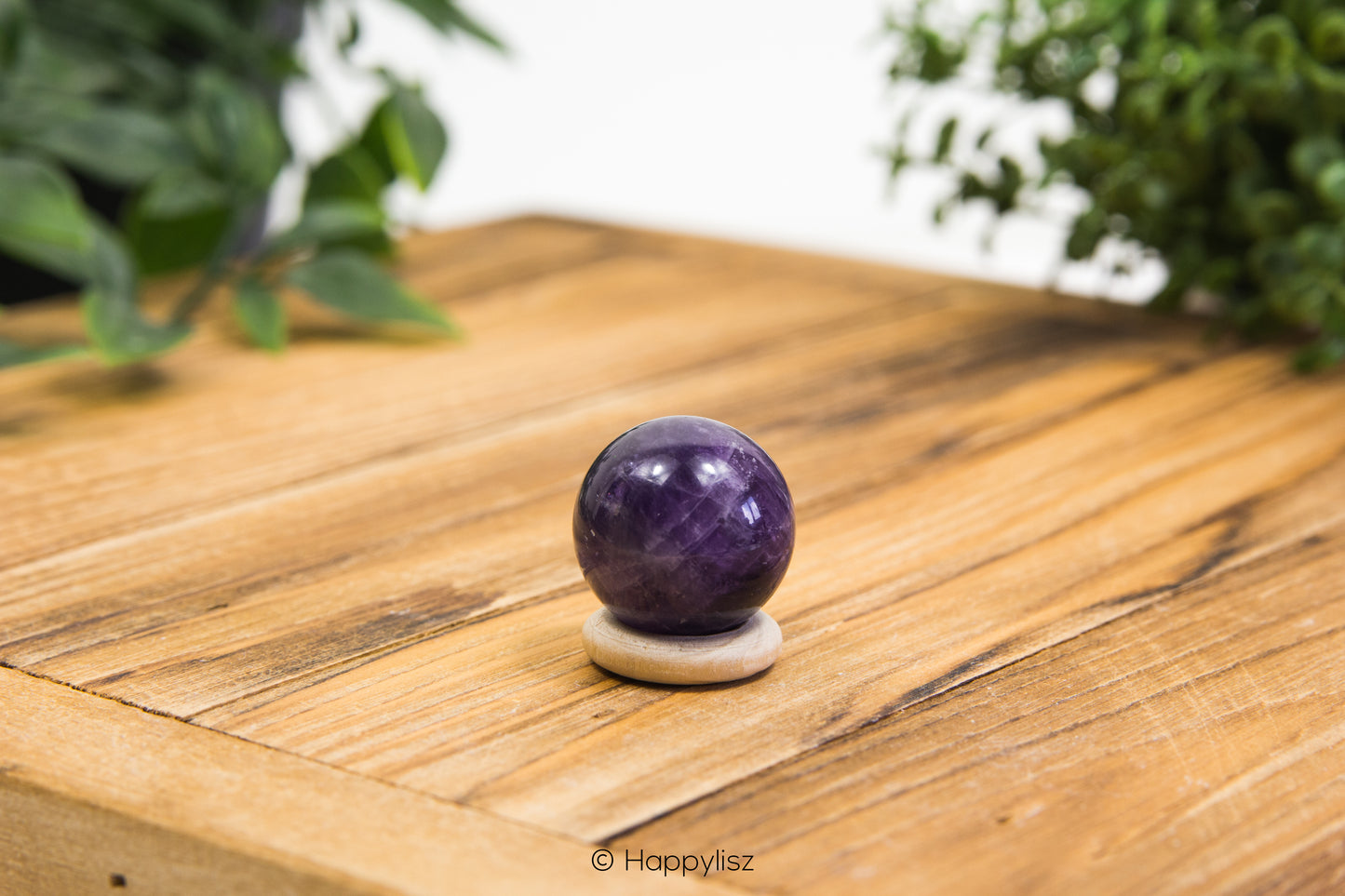 Purple crystal ball on a wooden surface with greenery in the background