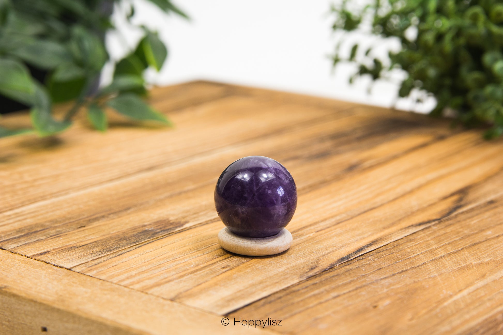 Amethyst crystal ball on a wooden surface with greenery in the background