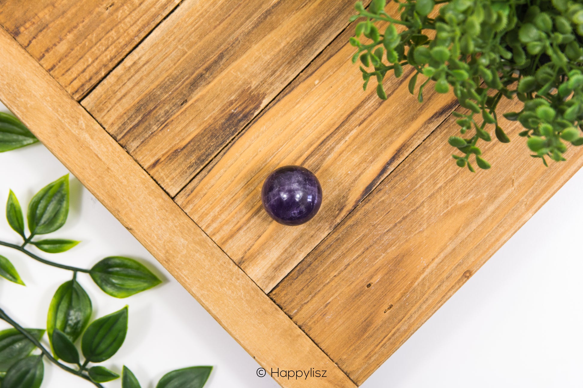 Wooden surface with a purple crystal ball and green leaves on a white background