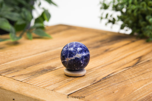 Sodalite sphere on a wooden surface with greenery in the background
