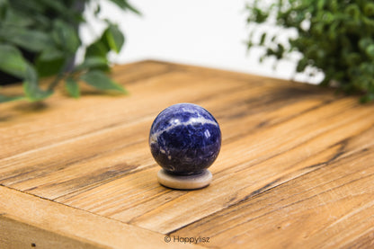 Sodalite spherical object on a wooden surface with greenery in the background